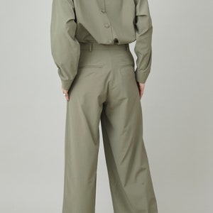May include: A sage green button-down shirt with a high collar and long sleeves. The shirt has a row of buttons down the back. The model is also wearing sage green wide-leg pants.