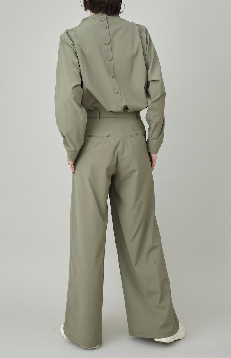 May include: A sage green button-down shirt with a high collar and long sleeves. The shirt has a row of buttons down the back. The model is also wearing sage green wide-leg pants.