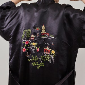 May include: Black satin robe with an embroidered design of a pagoda, trees, and flowers. The robe has a tie belt.