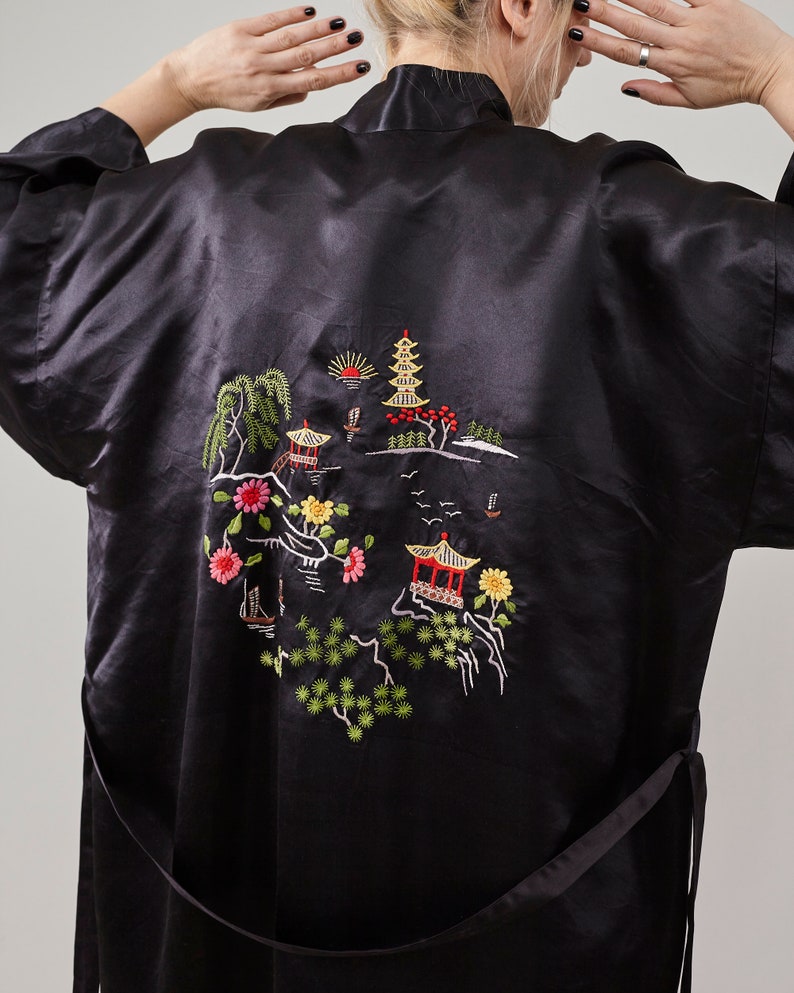 May include: Black satin robe with an embroidered design of a pagoda, trees, and flowers. The robe has a tie belt.