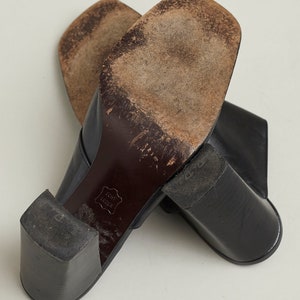 Puede incluir: Un par de zapatos de tac&oacute;n de cuero negro con punta cuadrada. Los zapatos tienen un tac&oacute;n grueso y est&aacute;n hechos de cuero genuino. Las suelas de los zapatos est&aacute;n gastadas y muestran signos de uso.