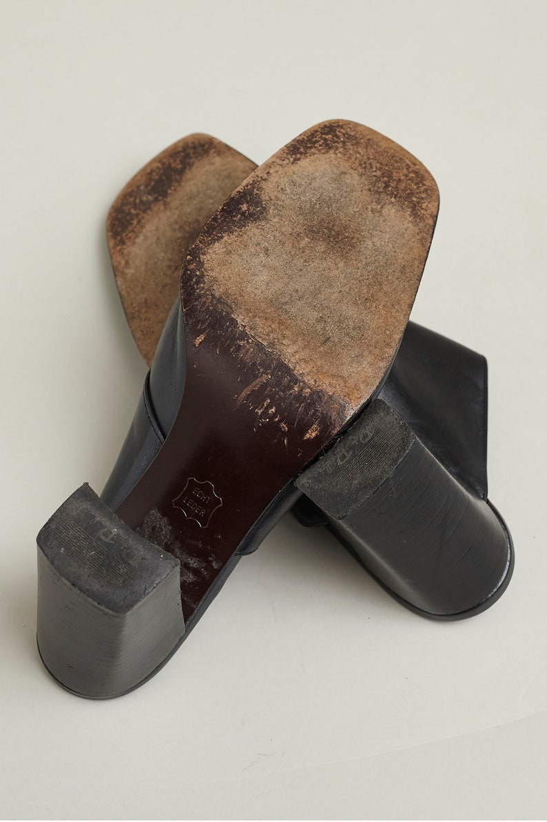 Puede incluir: Un par de zapatos de tac&oacute;n de cuero negro con punta cuadrada. Los zapatos tienen un tac&oacute;n grueso y est&aacute;n hechos de cuero genuino. Las suelas de los zapatos est&aacute;n gastadas y muestran signos de uso.