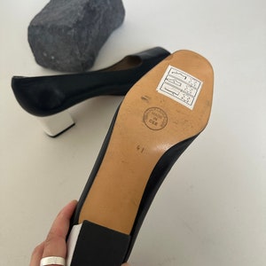 K&ouml;nnte beinhalten: Schwarze Lederschuhe mit einer wei&szlig;en Plattform und einem Blockabsatz. Die Schuhe haben ein Gr&ouml;&szlig;enetikett 41 auf der Sohle und ein Etikett mit der Aufschrift "Leather Leather Club Made in CEE".