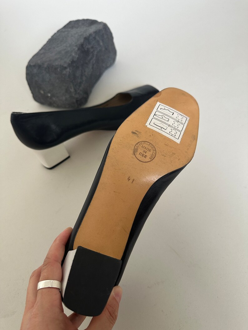 K&ouml;nnte beinhalten: Schwarze Lederschuhe mit einer wei&szlig;en Plattform und einem Blockabsatz. Die Schuhe haben ein Gr&ouml;&szlig;enetikett 41 auf der Sohle und ein Etikett mit der Aufschrift "Leather Leather Club Made in CEE".