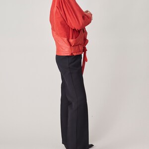 May include: A red suede jacket with a belted waist and a black pair of pants.