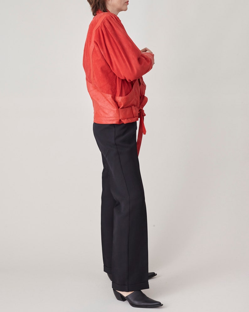 May include: A red suede jacket with a belted waist and a black pair of pants.
