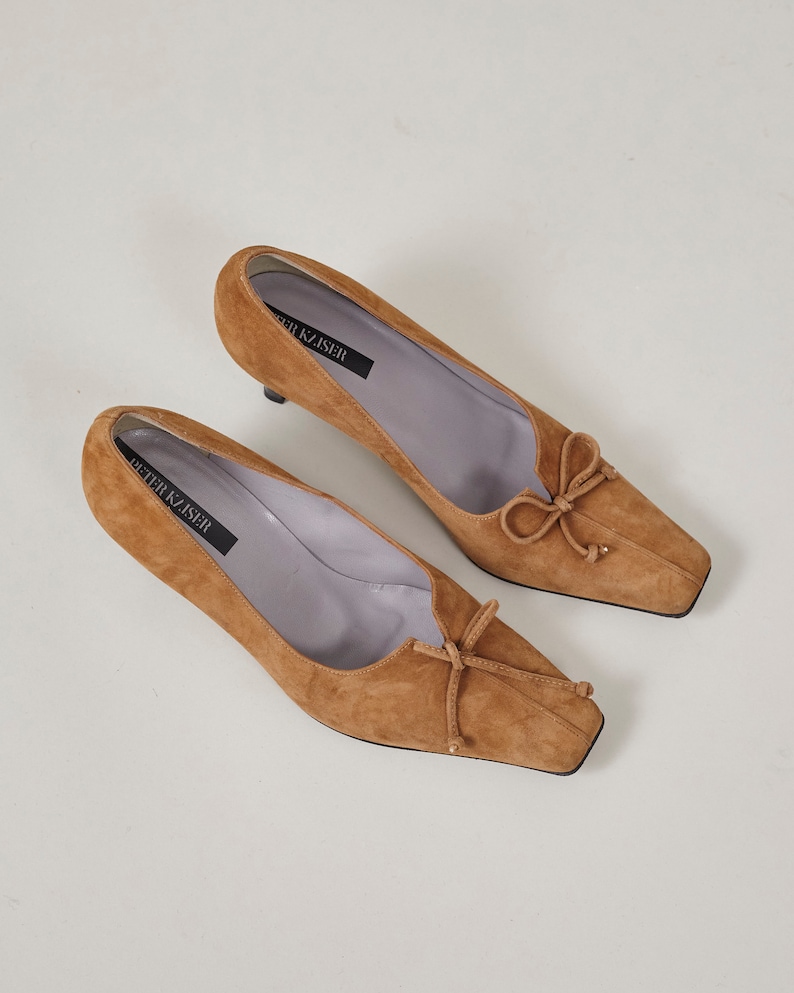 K&ouml;nnte beinhalten: Ein Paar braune Wildlederschuhe mit Absatz, quadratischer Spitze und Schleife an der Vorderseite. Die Schuhe sind auf der Innensohle mit "Peter Kaiser" gekennzeichnet.