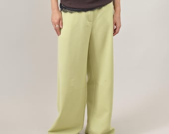 May include: Light green wide-leg pants. The pants have a high waist and a relaxed fit. The model is wearing a dark brown long-sleeve shirt with a black lace trim. The pants are paired with brown leather loafers.