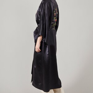 May include: A long black satin robe with floral embroidery on the back. The robe has a sash tie at the waist and long sleeves.