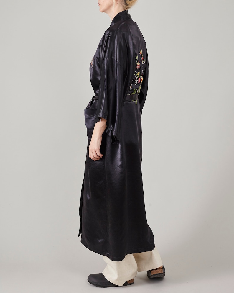 May include: A long black satin robe with floral embroidery on the back. The robe has a sash tie at the waist and long sleeves.
