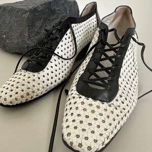 May include: A pair of white and black woven leather shoes with black laces. The shoes have a square toe and a low heel.