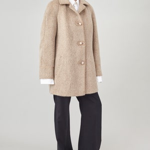May include: A beige wool coat with a notched collar and a row of buttons down the front. The coat has a slightly oversized fit and a straight hemline.