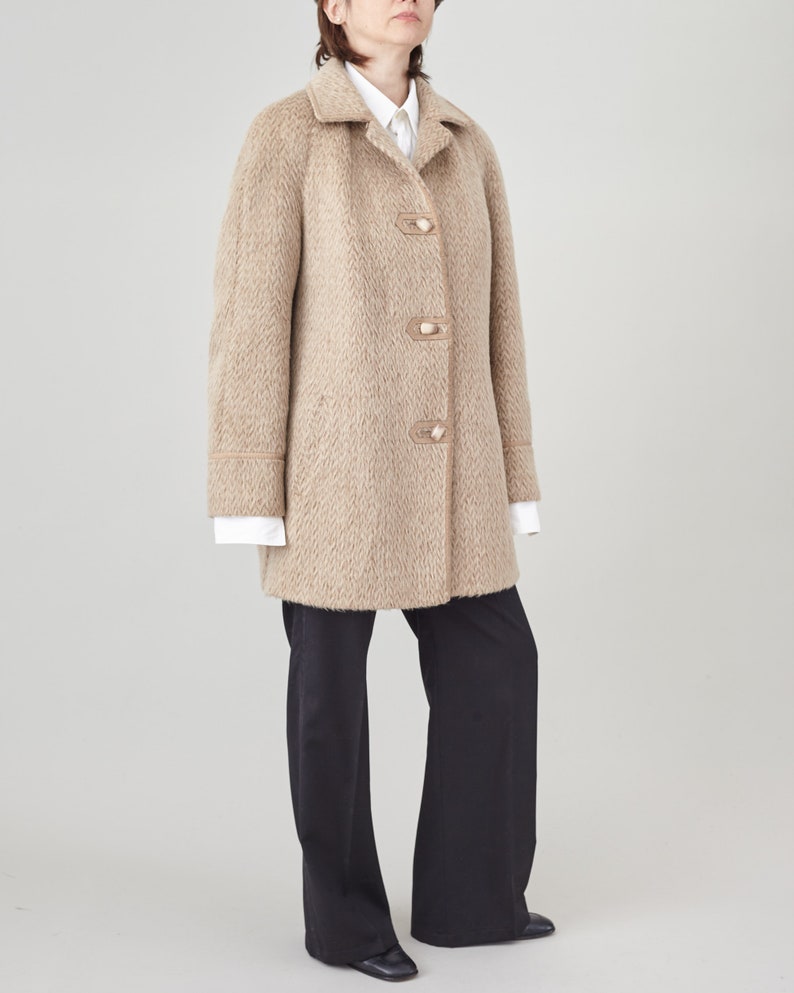 May include: A beige wool coat with a notched collar and a row of buttons down the front. The coat has a slightly oversized fit and a straight hemline.