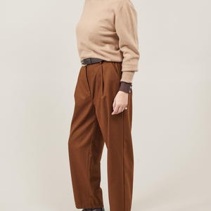 May include: A brown turtleneck sweater with a brown leather belt and brown pants. The person is wearing black heeled shoes.