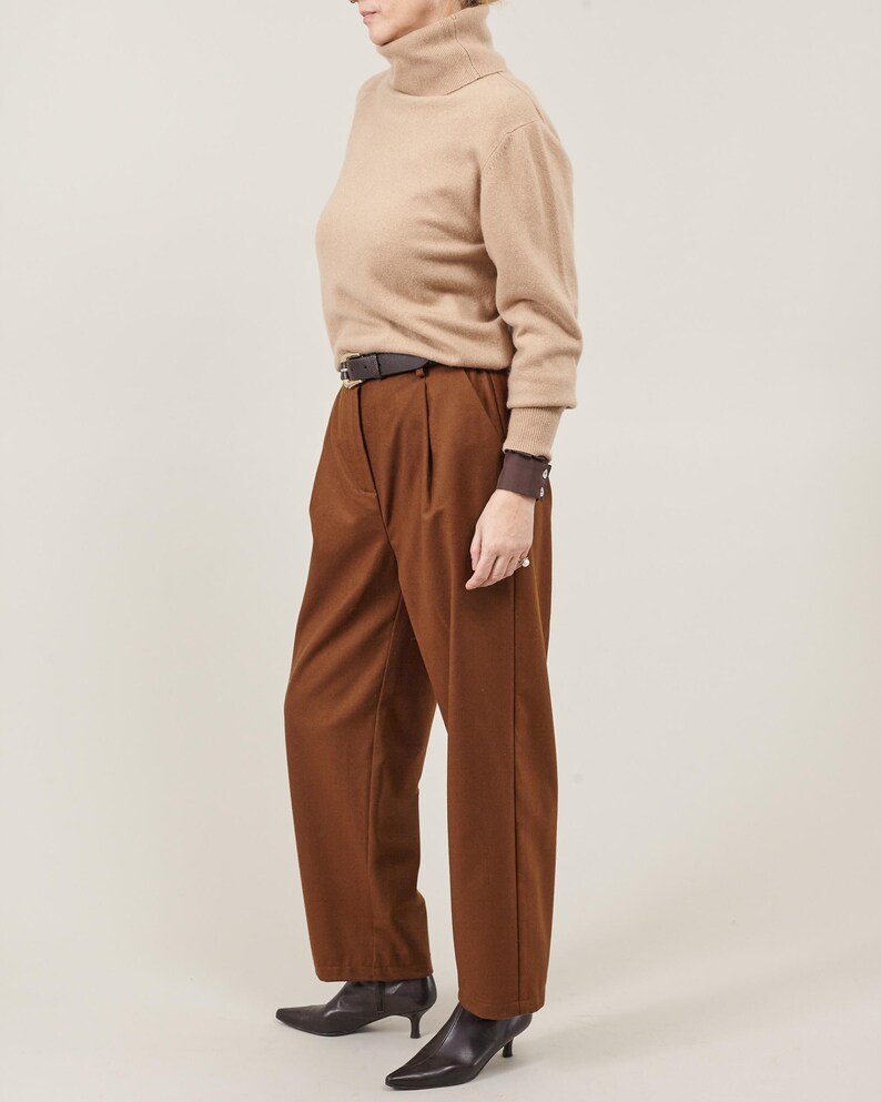 May include: A brown turtleneck sweater with a brown leather belt and brown pants. The person is wearing black heeled shoes.