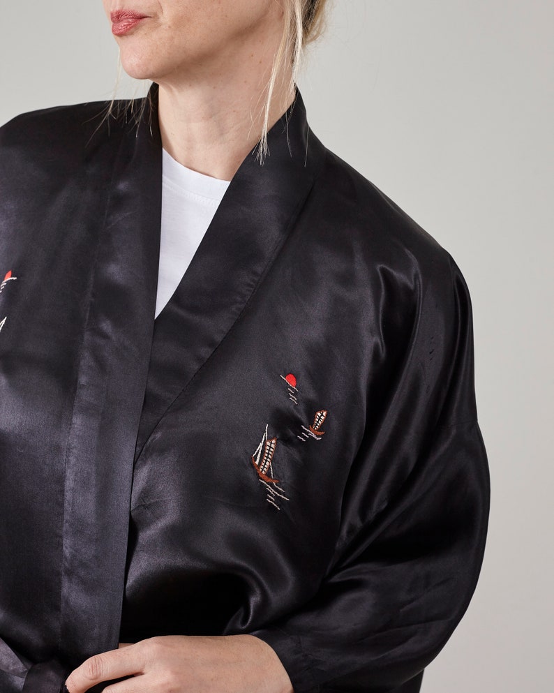May include: A black satin robe with embroidered sailboats and a red sun. The robe has a shawl collar and long sleeves.