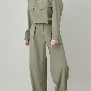 May include: A sage green pantsuit with a collared shirt and wide-leg pants. The shirt has a single pocket on the chest and the pants have a high waist.