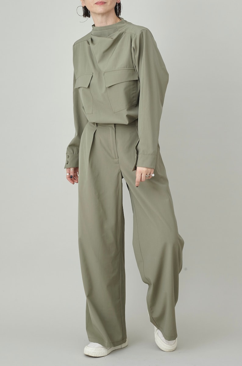 May include: A sage green pantsuit with a collared shirt and wide-leg pants. The shirt has a single pocket on the chest and the pants have a high waist.