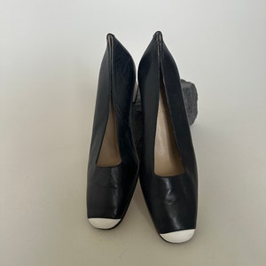 K&ouml;nnte beinhalten: Ein Paar schwarze Lederschuhe mit Absatz und wei&szlig;en Zehenkappen.