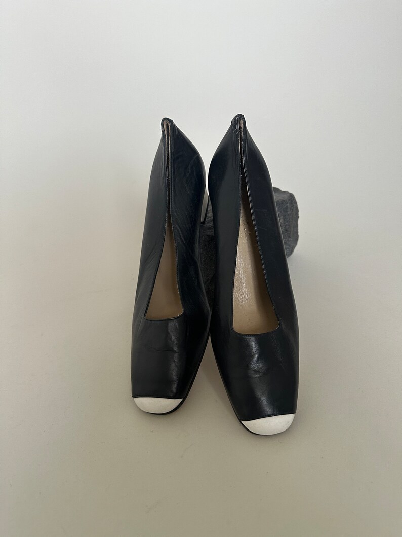 K&ouml;nnte beinhalten: Ein Paar schwarze Lederschuhe mit Absatz und wei&szlig;en Zehenkappen.