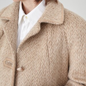 May include: A beige wool coat with a suede trim around the collar and pockets. The coat has a button closure and a textured woven pattern.