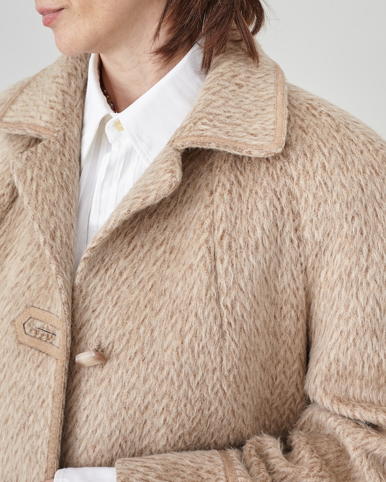 May include: A beige wool coat with a suede trim around the collar and pockets. The coat has a button closure and a textured woven pattern.