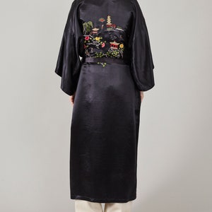 May include: A black satin robe with an embroidered design of a pagoda and flowers. The robe has a black sash.