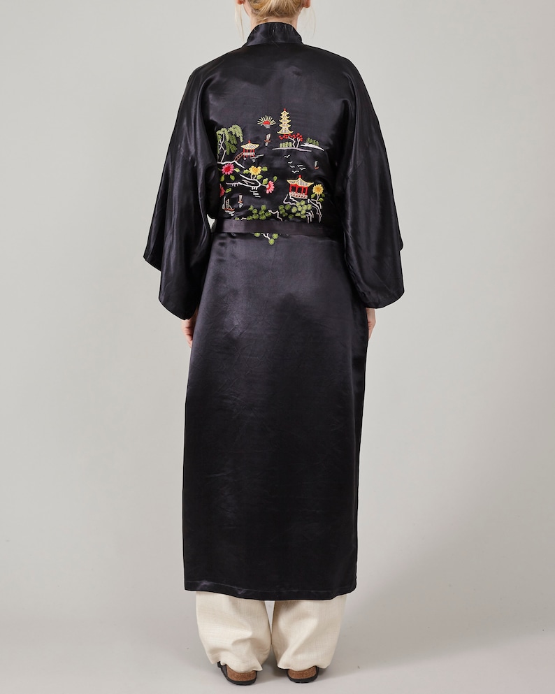 May include: A black satin robe with an embroidered design of a pagoda and flowers. The robe has a black sash.