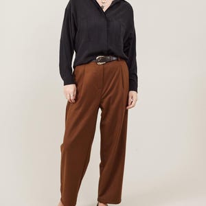 May include: A woman wearing a black button-down shirt with a brown belt and brown wide-leg pants. She is wearing brown and black leopard print flats.