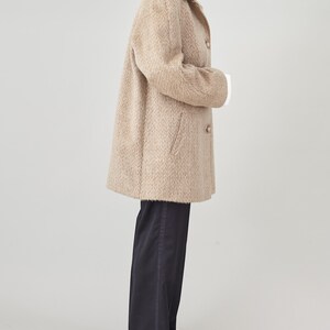May include: A beige long-sleeved coat with a button closure and a slightly oversized fit. The coat is made of a soft, fuzzy material and has a herringbone pattern.