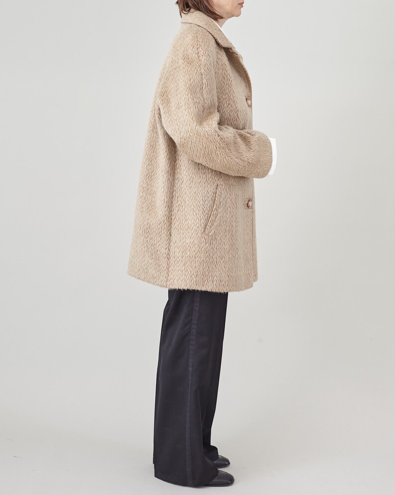 May include: A beige long-sleeved coat with a button closure and a slightly oversized fit. The coat is made of a soft, fuzzy material and has a herringbone pattern.