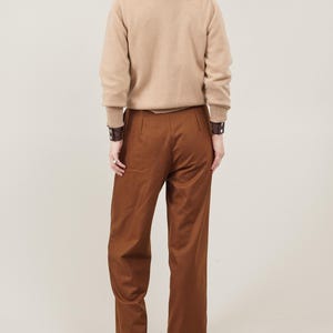May include: A brown turtleneck sweater with long sleeves and a pair of brown wide-leg pants. The person is wearing brown leather bracelets on both wrists.