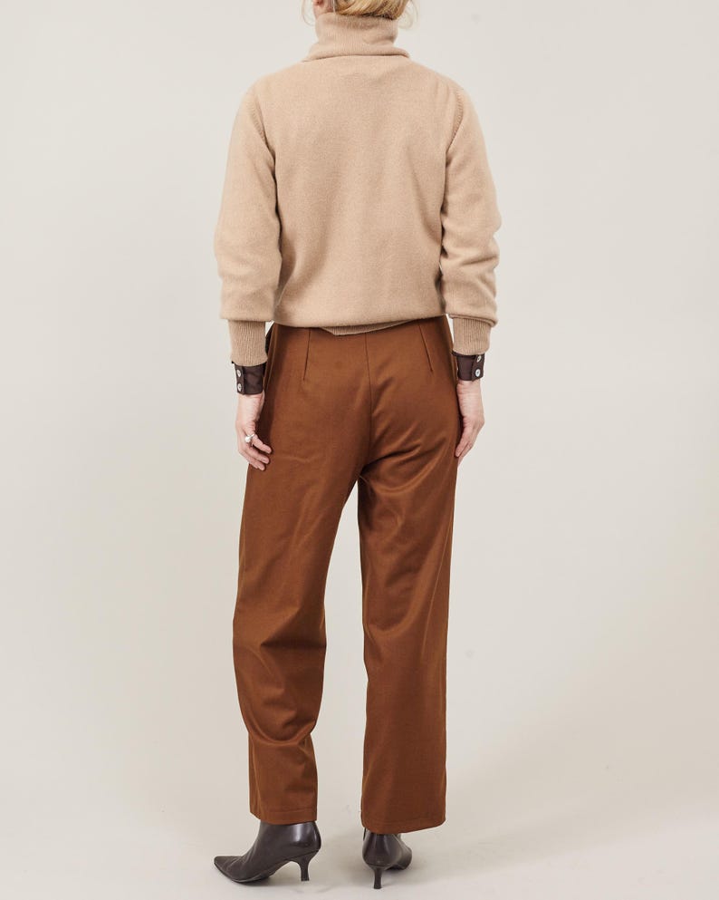 May include: A brown turtleneck sweater with long sleeves and a pair of brown wide-leg pants. The person is wearing brown leather bracelets on both wrists.