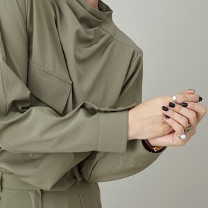 May include: A green, long-sleeved shirt with a high neckline and a single pocket on the left side. The shirt is made of a soft, wrinkle-resistant fabric.