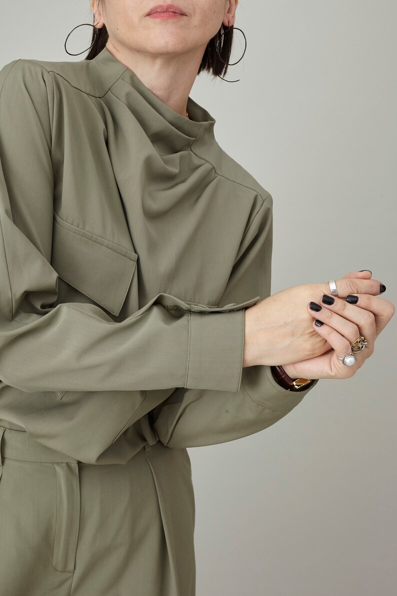 May include: A green, long-sleeved shirt with a high neckline and a single pocket on the left side. The shirt is made of a soft, wrinkle-resistant fabric.