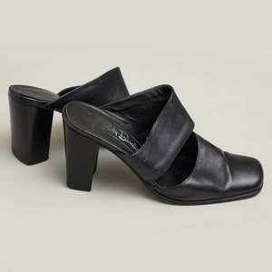 Puede incluir: Mulas de tac&oacute;n de cuero negro con puntera cuadrada y dos tiras en la parte superior. Los zapatos est&aacute;n etiquetados como "Betty Barclay".