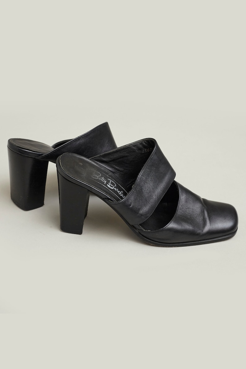 Puede incluir: Mulas de tac&oacute;n de cuero negro con puntera cuadrada y dos tiras en la parte superior. Los zapatos est&aacute;n etiquetados como "Betty Barclay".
