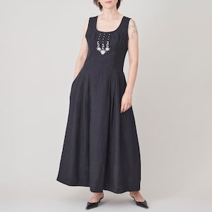 May include: A black sleeveless maxi dress with a white embroidered neckline and a silver necklace. The dress has a fitted bodice and a flowing skirt.