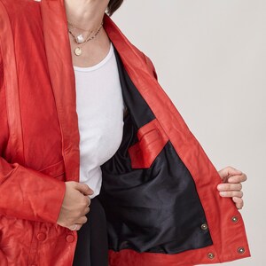 May include: A red leather jacket with a black lining and a button closure. The jacket has a collar and long sleeves.