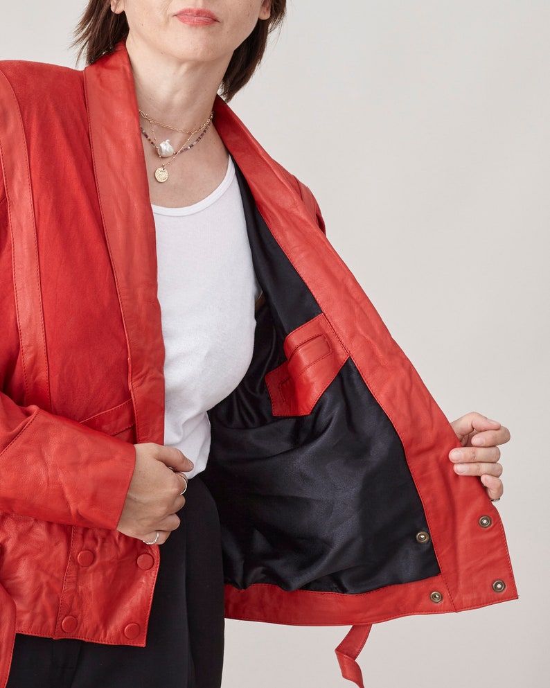May include: A red leather jacket with a black lining and a button closure. The jacket has a collar and long sleeves.