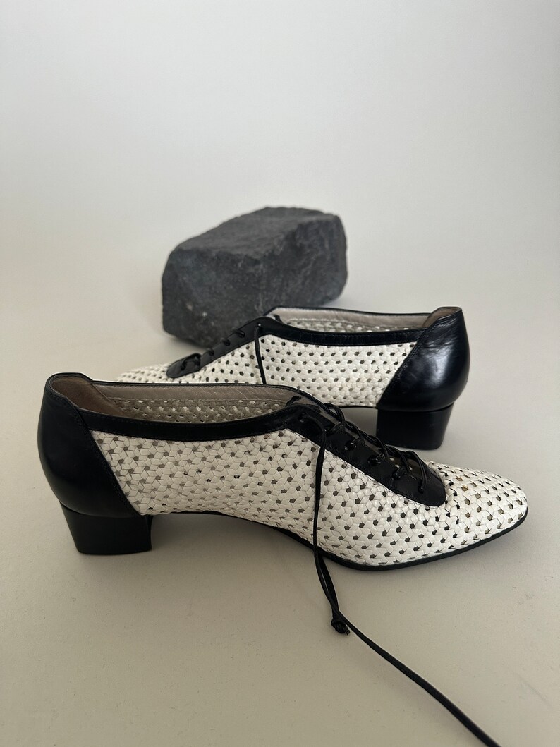 May include: White and black woven leather shoes with a lace-up closure and a low block heel.