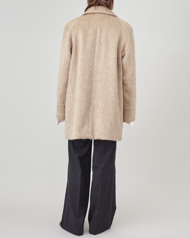 May include: A beige wool coat with a long, relaxed fit. The coat has a notched collar, a button closure, and long sleeves. The coat is shown from the back.