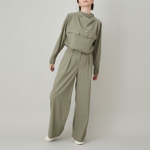 May include: A green long-sleeved shirt with a high collar and a single pocket on the chest. The shirt is paired with matching green wide-leg pants.