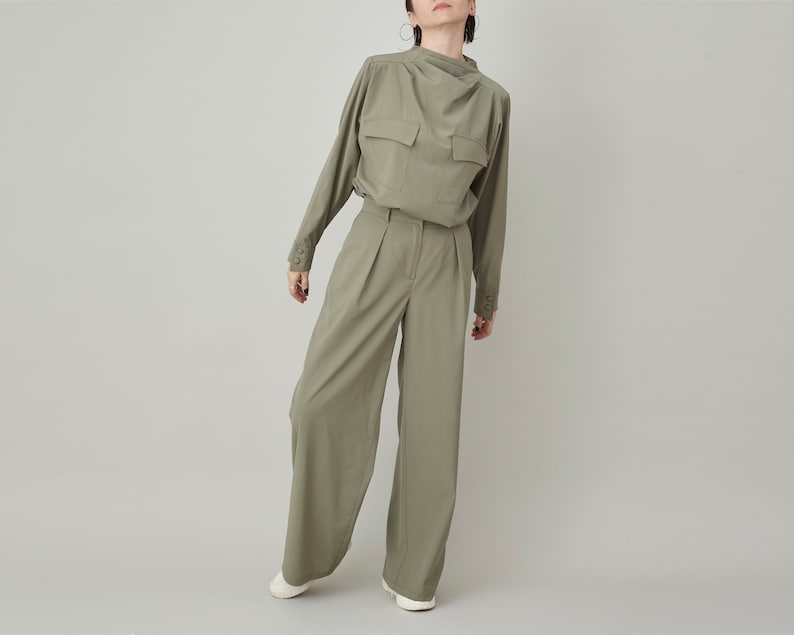 May include: A green long-sleeved shirt with a high collar and a single pocket on the chest. The shirt is paired with matching green wide-leg pants.