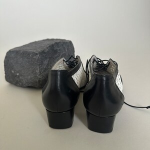 May include: A pair of black and white lace-up shoes with a low heel. The shoes have a woven pattern on the upper part and a solid black leather heel.