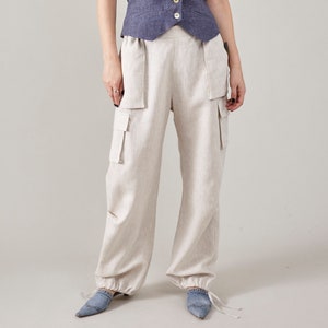 Pode incluir: Calça cargo de linho bege com perna larga e cordão de ajuste na parte inferior. A calça tem vários bolsos e um ajuste ligeiramente solto.