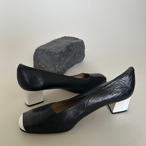 K&ouml;nnte beinhalten: Paar schwarze Lederschuhe mit Absatz und wei&szlig;em Besatz an Zehen und Absatz.