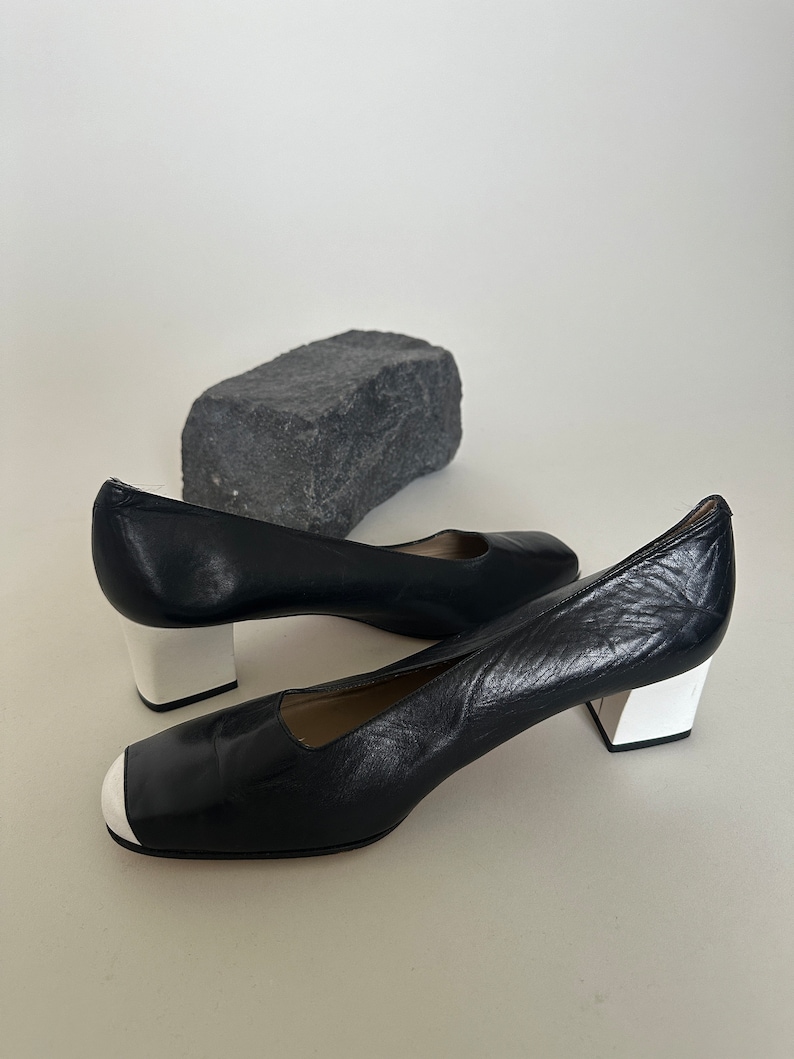K&ouml;nnte beinhalten: Paar schwarze Lederschuhe mit Absatz und wei&szlig;em Besatz an Zehen und Absatz.