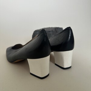 K&ouml;nnte beinhalten: Ein Paar schwarze Lederschuhe mit wei&szlig;en Abs&auml;tzen. Die Schuhe haben eine spitze Zehenpartie und einen niedrigen Absatz.