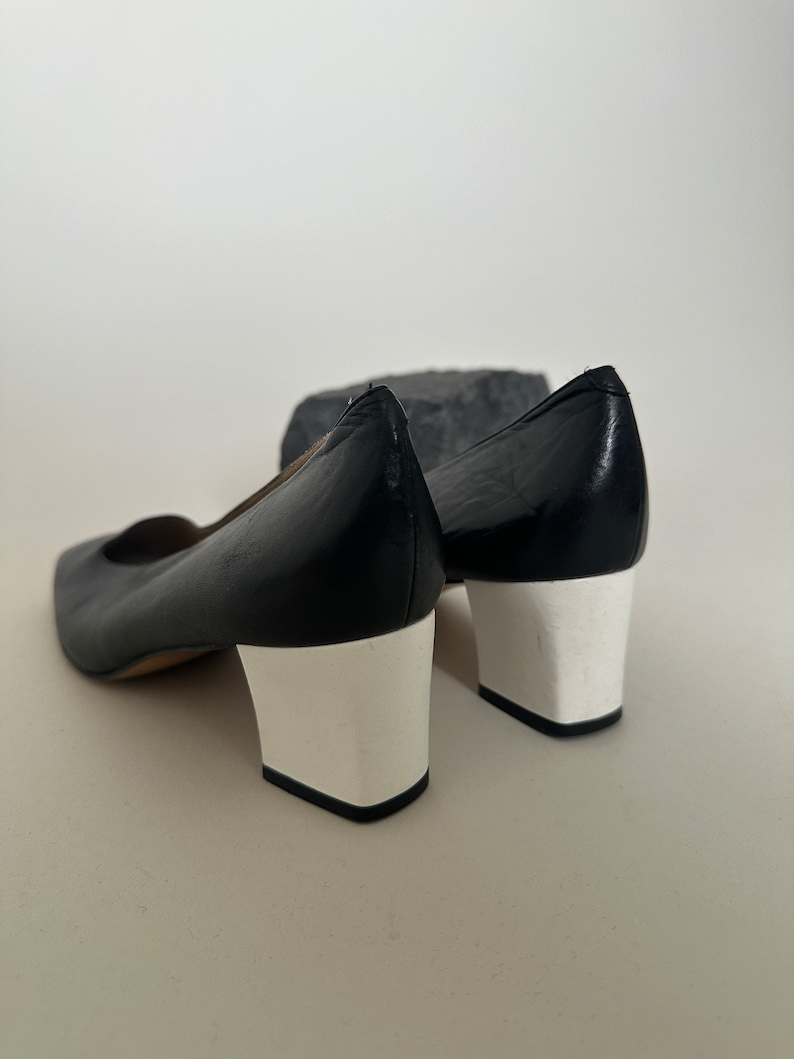 K&ouml;nnte beinhalten: Ein Paar schwarze Lederschuhe mit wei&szlig;en Abs&auml;tzen. Die Schuhe haben eine spitze Zehenpartie und einen niedrigen Absatz.